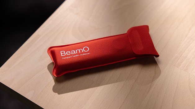 A red fabric pouch labeled 'BeamO Compact health multiscan' resting on a wooden surface.